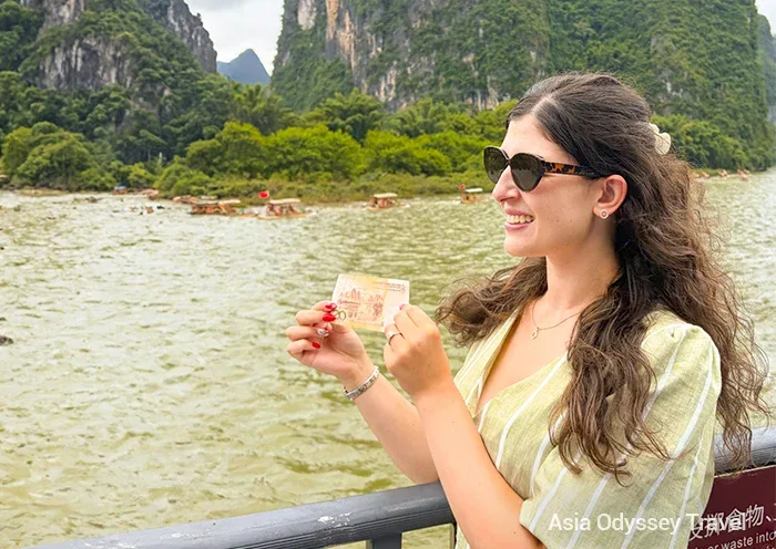 Turista sosteniendo un billete de 20 RMB en un crucero por el río Li entre montañas cársticas de Yangshuo